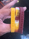 The Washington Redskins Adult Mylar NFL Team Logo + Color 3pk Wristbands Bracelet is a set of three wristbands featuring the iconic team logo and colors of the Washington Commanders.